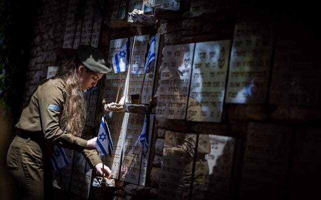 An Israeli soldier places flags on graves of fallen soldiers at the Mount Herzl Military Cemetery in Jerusalem, April 23, 2023, ahead of Memorial Day. (Yonatan Sindel/Flash90)