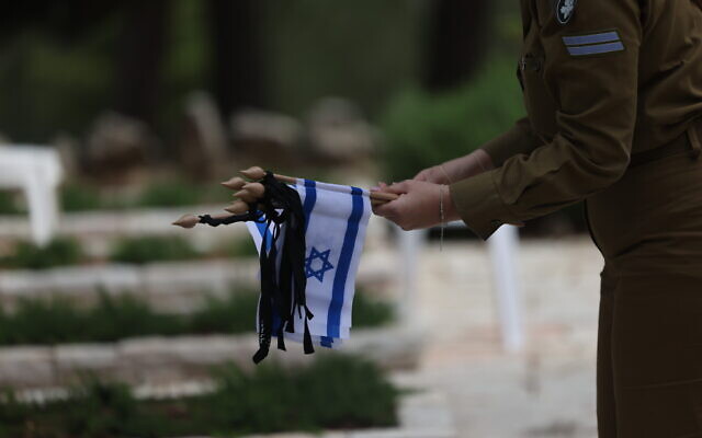 An IDF soldier places flags on graves of fallen soldiers at the military cemetery at Mount Herzl in Jerusalem, April 23, 2023, ahead of Memorial Day. (Yonatan Sindel/Flash90)