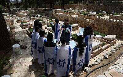 People wearing Israeli flags visit Mount Herzl Military Cemetery in Jerusalem, on April 23, 2023, ahead of Memorial Day. (Yonatan Sindel/Flash90)
