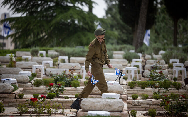 An Israeli soldier places flags, flowers and candles on graves of fallen soldiers at the Mount Herzl Military Cemetery in Jerusalem, April 23, 2023, ahead of Memorial Day. (Yonatan Sindel/Flash90) An Israeli soldier places flags, flowers and candles on graves of fallen soldiers at the Mount Herzl Military Cemetery in Jerusalem, April 23, 2023, ahead of Memorial Day. (Yonatan Sindel/Flash90)
