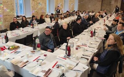 Guests at a seder in Kyiv, Ukraine, including many families from heavily damaged Kharkiv, sit around the seder table on the first night of Passover, April 5, 2023. (Marcel Gascon Barbera/JTA)