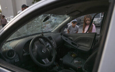 Israeli children look at a damaged car in the southern city of Sderot following rocket fire from Gaza on May 2, 2023 (AHMAD GHARABLI / AFP)