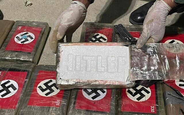 In this photo provided by the Peruvian Anti-Drug Police, an officer shows blocks of cocaine marked with Nazi swastikas and stamped with the name "HITLER", at the port of Paita, Piura region, Peru, Thursday, May 25, 2023.  (Peruvian Anti-Drug Police via AP)