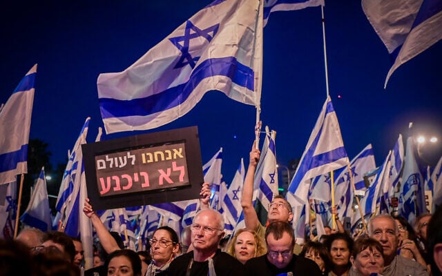 A protester holds a sign saying 'We will never surrender' at a rally against the planned judicial overhaul in Tel Aviv, on June 3, 2023 (Avshalom Sassoni/Flash90) A protester holds a sign saying 'We will never surrender' at a rally against the planned judicial overhaul in Tel Aviv, on June 3, 2023 (Avshalom Sassoni/Flash90)