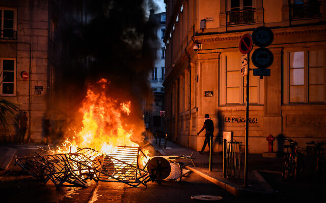 Smoke rises from a bonfire near a graffiti reading 'The police kills' during clashes with police in the streets of Lyon, south-eastern France, on June 30, 2023, three days after a 17-year-old boy was shot in the chest by police at point-blank range in Nanterre, a western suburb of Paris (JEFF PACHOUD / AFP)