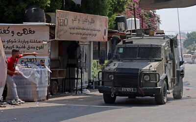 A Palestinian throws a stone at an armored IDF vehicle during a military operation in the northern West Bank city of Jenin, July 3, 2023. (Jaafar Ashtiyeh/ AFP)