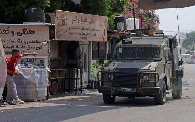 A Palestinian throws a stone at an armored IDF vehicle during a military operation in the northern West Bank city of Jenin, July 3, 2023. (Jaafar Ashtiyeh/ AFP) A Palestinian throws a stone at an armored IDF vehicle during a military operation in the northern West Bank city of Jenin, July 3, 2023. (Jaafar Ashtiyeh/ AFP)