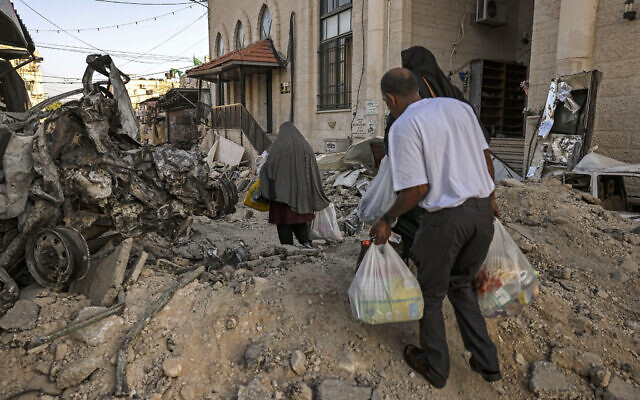 People carry bags with goods given by a local organization as they walk among debris in the aftermath of an IDF military operation in the Jenin refugee camp in the West Bank on July 5, 2023. (Photo by RONALDO SCHEMIDT / AFP)