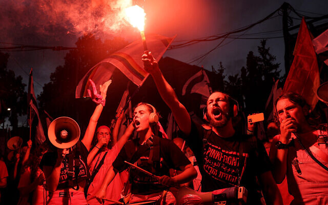 A demonstrator from the 'Pink Front' group lights a flare while others in a marching band perform with drums during a protest against the Israeli government's judicial overhaul plan in Tel Aviv on July 8, 2023. (JACK GUEZ / AFP)
