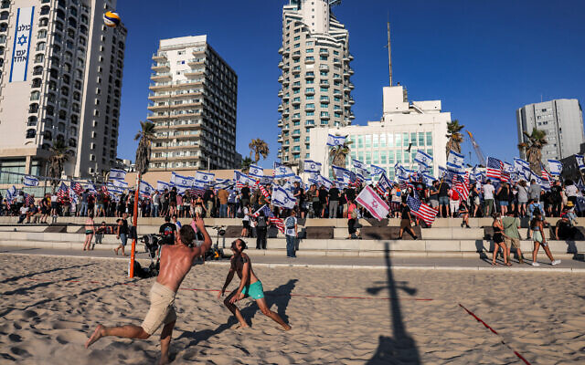 Men play beach volleyball as demonstrators protest against the judicial overhaul, outside the US embassy branch office in Tel Aviv, July 11, 2023. (Menahem Kahana/AFP)