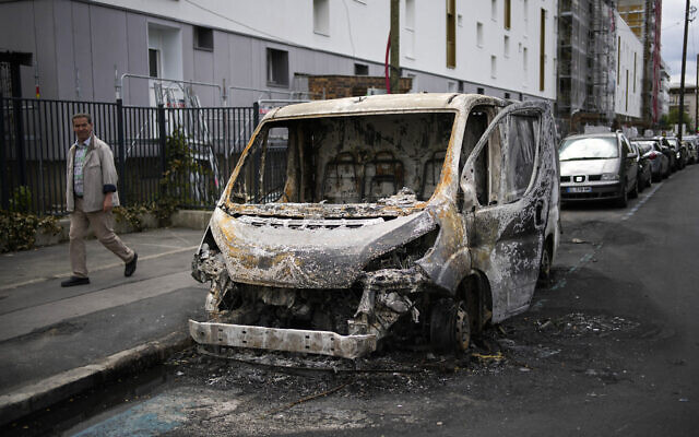 A man walks past a burned van on the aftermath of protests in Colombes, outside Paris, Saturday, July 1, 2023. (AP/Christophe Ena)