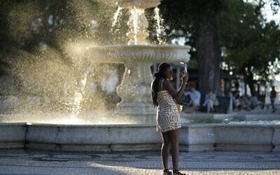 A woman takes pictures by a fountain at a public garden in Lisbon, as the sun sets, Monday, July 3, 2023. (AP/Armando Franca)