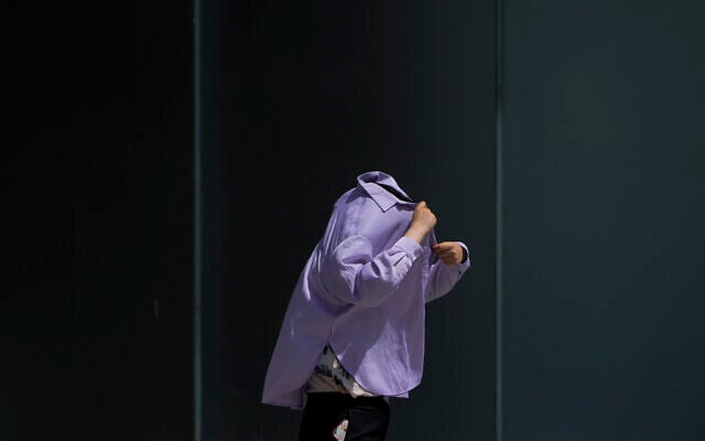 A woman uses a long-sleeve shirt to shield from the sun as she walks at an outdoor shopping mall on a sweltering day in Beijing, July 6, 2023. (Andy Wong/AP) A woman uses a long-sleeve shirt to shield from the sun as she walks at an outdoor shopping mall on a sweltering day in Beijing, July 6, 2023. (Andy Wong/AP)