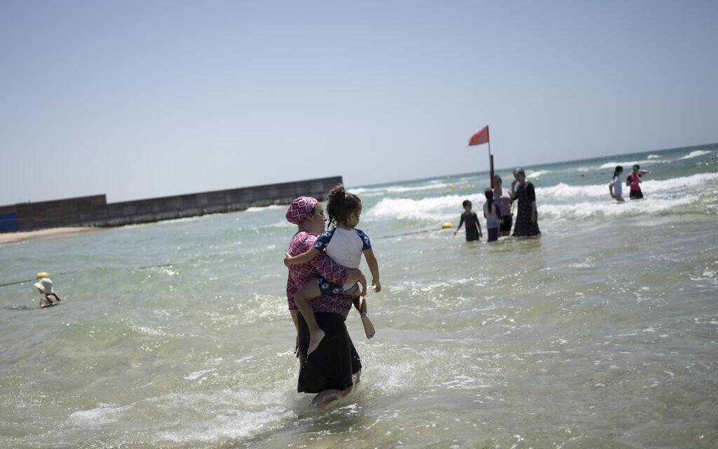A woman holds her child as religious and secular women take refuge from a summer heat wave at a public beach on one of three days in the week designated for women in Ashdod, Israel on Thursday, July 13, 2023. (AP/Maya Alleruzzo)