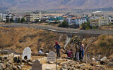 Residents dig a grave at a cemetery on the Lebanese side of the Lebanese-Israeli border in the southern village of Wazzani with the walled northern part of Ghajar village in the background, Lebanon, Tuesday, July 11, 2023. (AP Photo/Hassan Ammar)