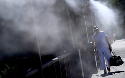 A man walks along a sidewalk under the misters, Friday, July 14, 2023 in downtown Phoenix. Phoenix hit 112 degrees on Friday, marking the city's 15th consecutive day of 110 degree-plus temperatures and putting it on track to beat the longest measured stretch of such heat.  (AP Photo/Matt York)