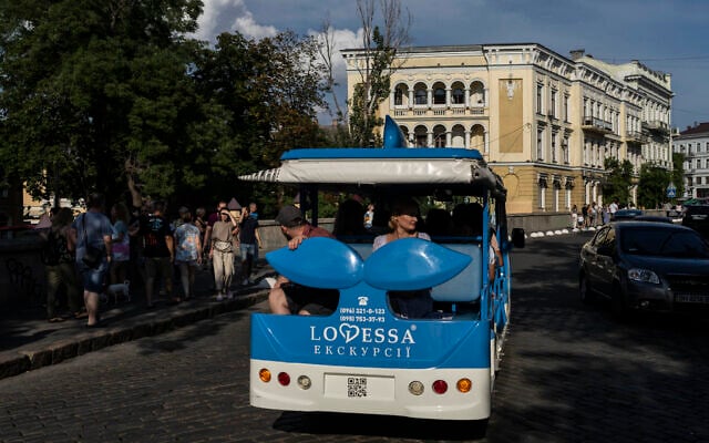 Tourists sit in a sightseeing bus as a small crowd gather on a bridge to view buildings destroyed in Russian missile attacks in Odesa, Ukraine, July 23, 2023. (Jae C. Hong/AP)