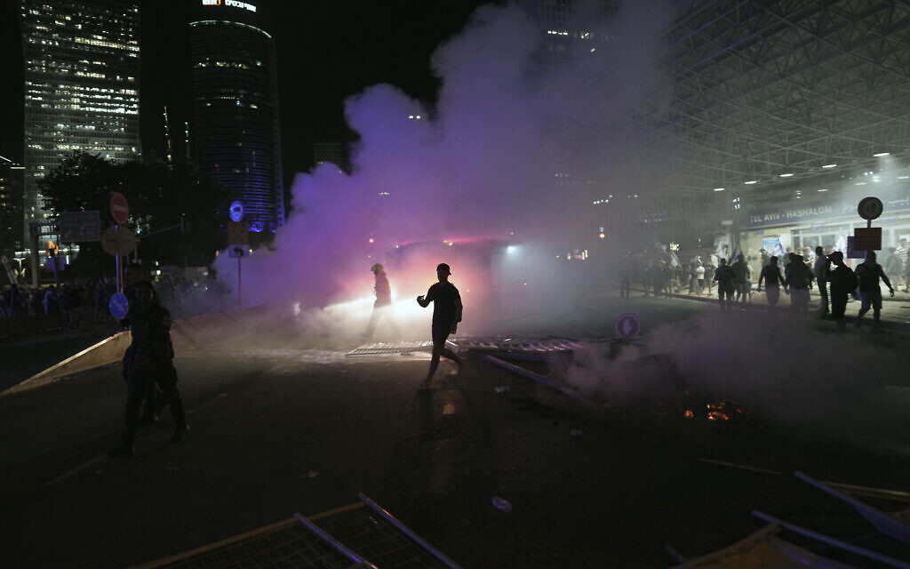 A man runs through smoke during a protest against plans by Netanyahu's government to overhaul the judicial system, in Tel Aviv, Monday, July 24, 2023. (AP/Oded Balilty)