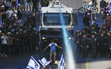 A protester stands in front of a police water cannon being used to disperse demonstrators blocking a road during a protest against moves by Prime Minister Benjamin Netanyahu's government to overhaul the judicial system, in Jerusalem, July 24, 2023. (AP/Ariel Schalit)