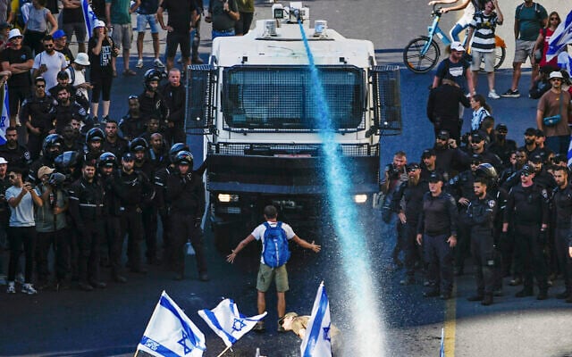 A protester stands in front of a police water cannon being used to disperse demonstrators blocking a road during a protest against moves by Prime Minister Benjamin Netanyahu's government to overhaul the judicial system, in Jerusalem, July 24, 2023. (AP/Ariel Schalit) A protester stands in front of a police water cannon being used to disperse demonstrators blocking a road during a protest against moves by Prime Minister Benjamin Netanyahu's government to overhaul the judicial system, in Jerusalem, July 24, 2023. (AP/Ariel Schalit)