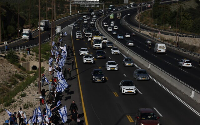 Demonstrators wave Israeli flags as they protest the government's judicial overhaul plans, by Route 1 near Ein Hemed, outside of Jerusalem, July 18, 2023. (Yonatan Sindel/Flash90) Demonstrators wave Israeli flags as they protest the government's judicial overhaul plans, by Route 1 near Ein Hemed, outside of Jerusalem, July 18, 2023. (Yonatan Sindel/Flash90)