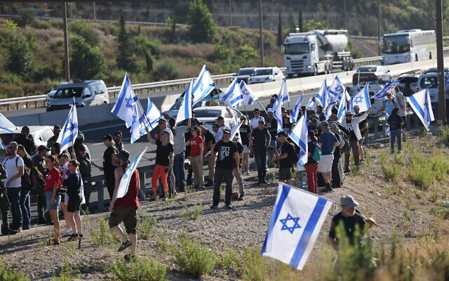 Demonstrators wave Israeli flags as they protest the government's judicial overhaul plans, by Route 1 near Ein Hemed, outside of Jerusalem, July 18, 2023. (Yonatan Sindel/Flash90) Demonstrators wave Israeli flags as they protest the government's judicial overhaul plans, by Route 1 near Ein Hemed, outside of Jerusalem, July 18, 2023. (Yonatan Sindel/Flash90)