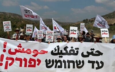 Left-wing activists marching toward Homesh, July 7, 2023, holding a sign reading 'Until Homesh is dismantled' in Hebrew and Arabic. (Courtesy Peace Now)