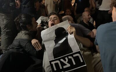 Demonstrator in Jerusalem holds sign reading "murderer" in Hebrew, depicting the acquitted officer who fatally shot Iyad Halak in 2020. (Charlie Summers/Times of Israel)