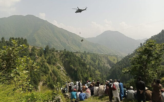 People watch as an army soldier slings down from a helicopter during a rescue mission to recover students stuck in a chairlift in Pashto village of mountainous Khyber Pakhtunkhwa province, on August 22, 2023. (AFP) People watch as an army soldier slings down from a helicopter during a rescue mission to recover students stuck in a chairlift in Pashto village of mountainous Khyber Pakhtunkhwa province, on August 22, 2023. (AFP)