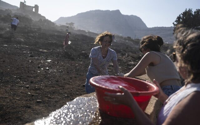 German tourists together with local residents try to extinguish a fire, near the seaside resort of Lindos, on the Aegean Sea island of Rhodes, southeastern Greece, on Monday, July 24, 2023. (AP Photo/Petros Giannakouris) German tourists together with local residents try to extinguish a fire, near the seaside resort of Lindos, on the Aegean Sea island of Rhodes, southeastern Greece, on Monday, July 24, 2023. (AP Photo/Petros Giannakouris)