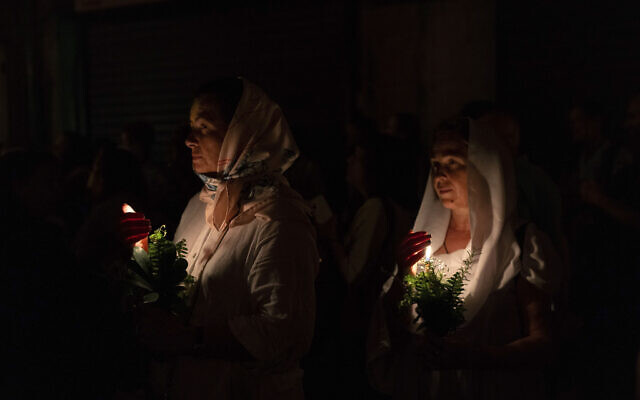 Christian orthodox women hold candles and flowers as they walk in a procession to bring an icon of the Virgin Mary to the tomb where it is believed she is buried, along the streets of the Old City of Jerusalem, early Friday, Aug. 25, 2023. Every year before the Feast of the Assumption, the icon is brought from the Church of the Holy Sepulchre to the tomb of the Virgin Mary to honor her Assumption. (AP/Ohad Zwigenberg)