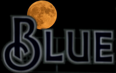 The full moon rises beyond a sign in the outfield during a baseball game between the Kansas City Royals and the Pittsburgh Pirates  in Kansas City, Missouri, on  August 30, 2023. (Charlie Riedel/AP)