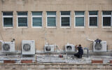 Illustrative: A worker installs air conditioners on the roof of an office building in central Jerusalem, on February 8, 2018. (Nati Shohat/Flash90)