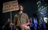 An anti-overhaul activist protesting in army duds in Tel Aviv, on August 12, 2023. His poster contains a slogan about bravery under fire. (Miriam Alster/Flash90)