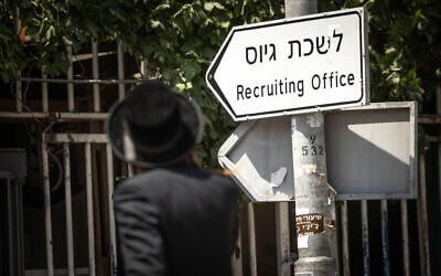 An ultra-Orthodox man walks past a sign for the IDF recruitment office in Jerusalem, August 16, 2023. (Chaim Goldberg/Flash90)
