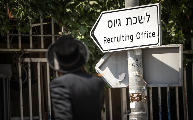 An ultra-Orthodox man walks past a sign for the IDF recruitment office in Jerusalem, August 16, 2023. (Chaim Goldberg/Flash90)