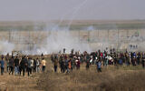 Palestinian protesters run to cover from tear gas during clashes with Israeli troops, along the frontier with Israel, east of Gaza City, Monday, August 21, 2023. (AP Photo/Adel Hana)