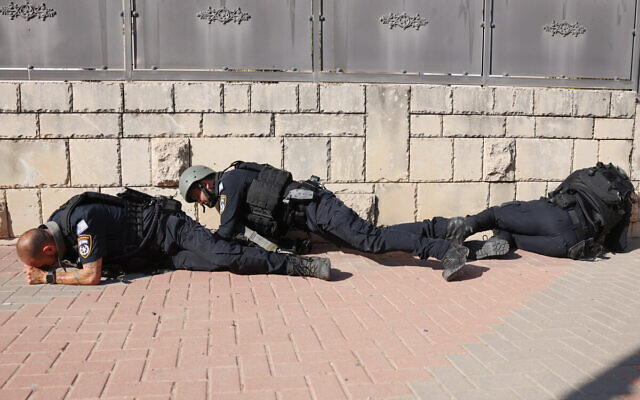 Israeli police forces take cover on the side of a street in Ashkelon as sirens wail while barrages of rockets are fired from the Gaza Strip into Israel on October 7, 2023. (AHMAD GHARABLI / AFP) Israeli police forces take cover on the side of a street in Ashkelon as sirens wail while barrages of rockets are fired from the Gaza Strip into Israel on October 7, 2023. (AHMAD GHARABLI / AFP)