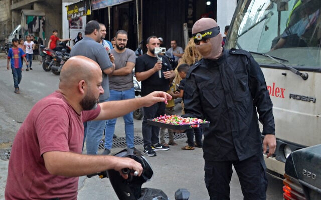 A member of the Al-Quds Brigades distributes candies in celebration of the deadly Hamas terror assault on Israel, at Lebanon's Beddawi refugee camp in Tripoli, Lebanon on October 7, 2023. (Fathi Al-Masri/AFP) A member of the Al-Quds Brigades distributes candies in celebration of the deadly Hamas terror assault on Israel, at Lebanon's Beddawi refugee camp in Tripoli, Lebanon on October 7, 2023. (Fathi Al-Masri/AFP)