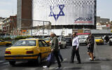People cross a road in front of an anti-Israel billboard with the checkered keffiyeh covering the Star of David, entitled, 'Operation Al-Aqsa Flood,' in solidarity with the Hamas operation against Israel, in Tehran's central Vali-Asr Square on October 8, 2023. (AFP)