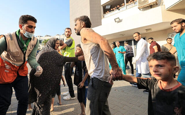A Palestinian man walks with a child while a woman comforts another outside al-Shifa hospital in Gaza City on October 12, 2023. (Mahmud Hams/AFP) A Palestinian man walks with a child while a woman comforts another outside al-Shifa hospital in Gaza City on October 12, 2023. (Mahmud Hams/AFP)