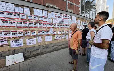 Supporters and family members of Israeli hostages look at images of the hostages plastered on a wall during a rally outside of the Kirya military base in central Tel Aviv on October 14, 2023. (Gil Cohen-Magen/AFP)