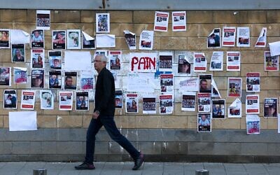 A man walks past images of Israeli hostages snatched by the Palestinian terror group Hamas last week during its devastating onslaught, plastered on a wall outside the Defense Ministry headquarters in Tel Aviv, on October 16, 2023. (AHMAD GHARABLI/AFP)