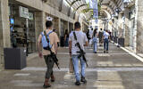 Illustrative: Israeli men, armed with US-made M16 automatic assault rifles, walk through the Mamilla shopping center in Jerusalem on October 25, 2023. (Yuri Cortez/AFP)