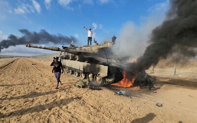 Palestinians celebrating, near a destroyed Israeli tank at the Gaza Strip fence east of Khan Younis, October 7, 2023. (AP/Hassan Eslaiah)