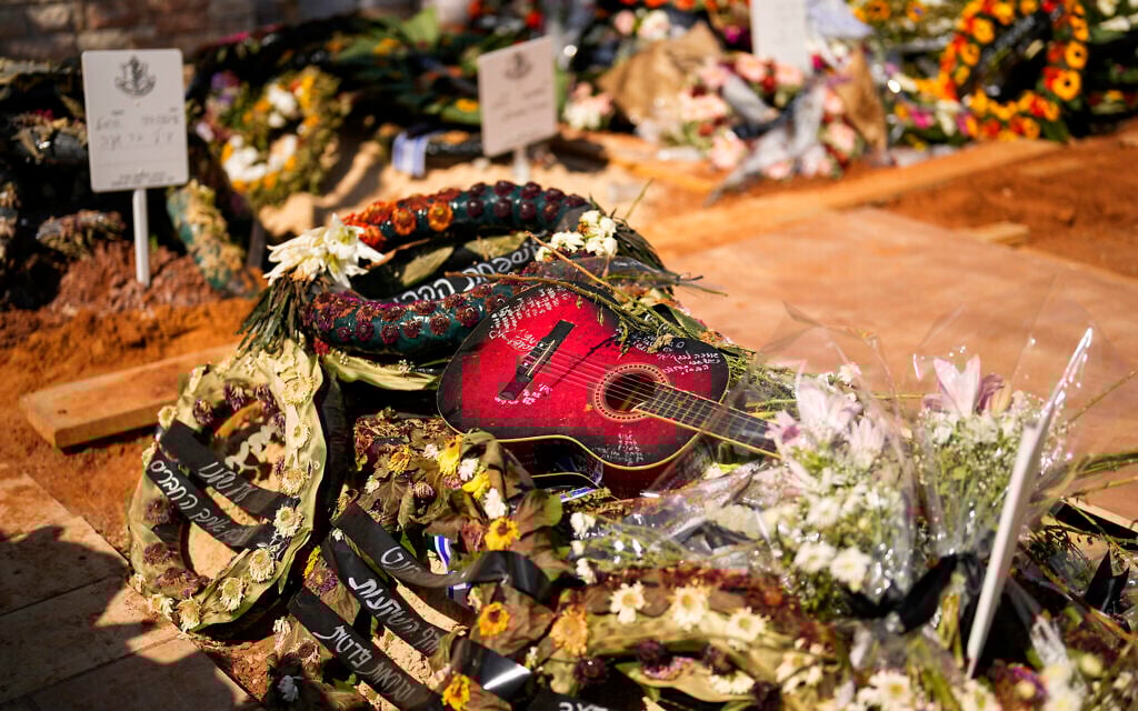 A guitar and flower wreaths are laid onto the grave of soldier Ilai Azar after his funeral at Kiryat Shaul cemetery in Tel Aviv, Israel, Saturday, Oct. 14, 2023. (AP Photo/Francisco Seco)