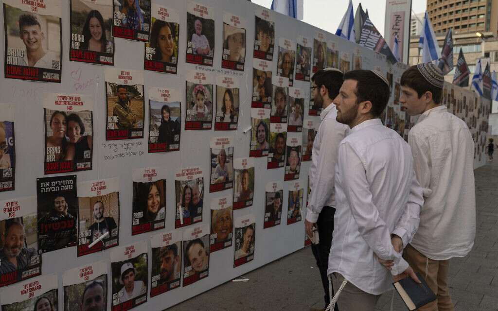 Young men look at photos of Israelis missing and held hostage in Gaza, displayed on a wall in Tel Aviv, on Friday, Oct. 20, 2023. (AP Photo/Petros Giannakouris)