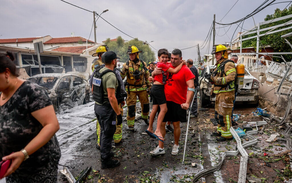 An Ashkelon resident and his son make their way to safety after a rocket fired from the Gaza Strip by Palestinian terrorists hit a building in the southern city, October 9, 2023 (Chaim Goldberg/Flash90)