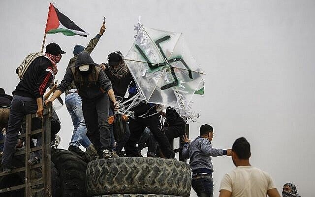 Illustrative: Palestinians hold a kite adorned with a swastika that is carrying a bomb near the border with Israel east of Gaza City, on April 20, 2018. (AFP Photo/Mohammed Abed)
