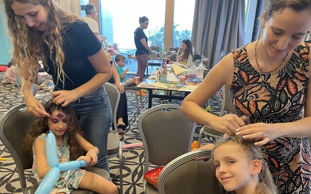 Ella Meskel (left) and Eva Volovik enjoy being made up by volunteers at the Herod's Hotel in Tel Aviv on October 9, 2023, after fleeing from missiles from Gaza and a gunfight between kibbutz members and Hamas terrorists on October 7. (Sue Surkes/Times of Israel)